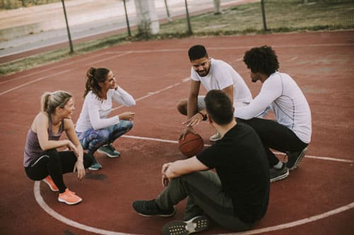 Grupo de pessoas sentadas em uma quadra de basquete, interagindo e desfrutando do ambiente esportivo.